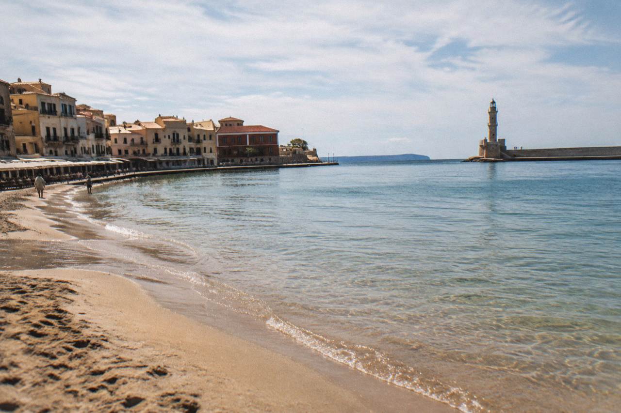 A sandy beach with calm shallow water beside a small town waterfront at midday