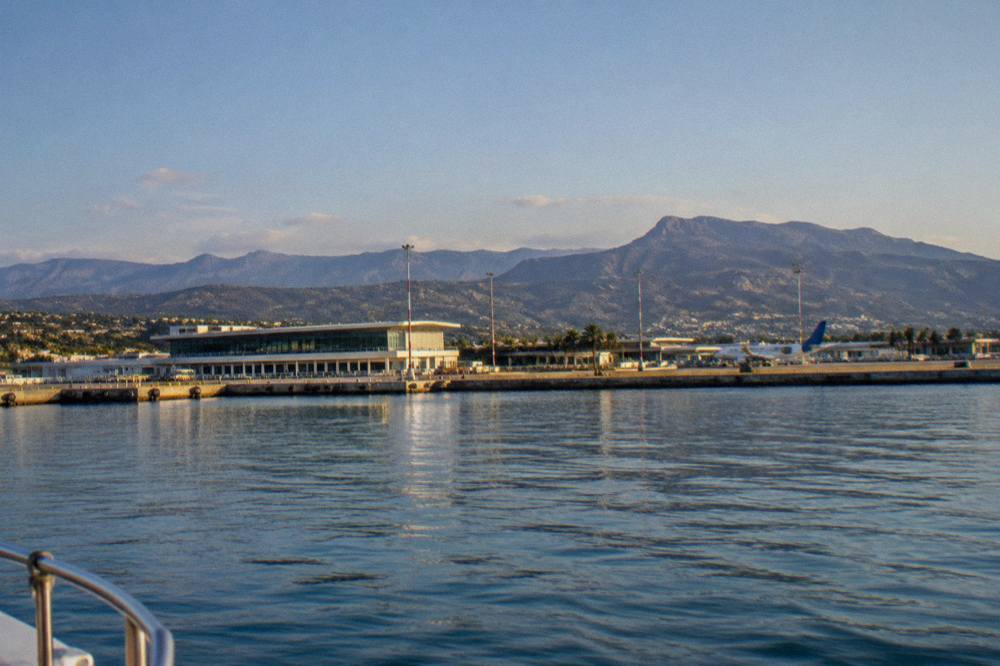 A calm bay with a port terminal and hills behind, seen from the water in morning light