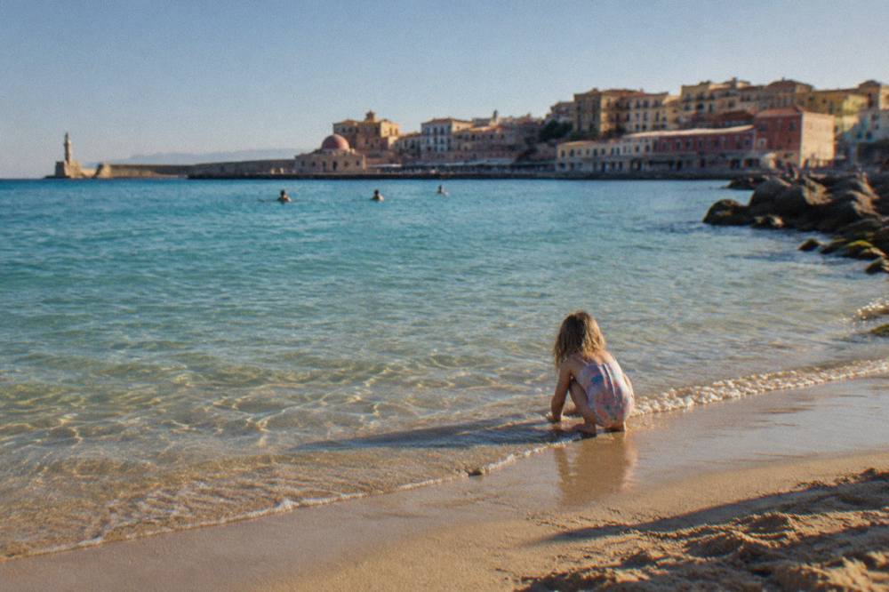 A calm shallow lagoon at a sandy beach near Chania with turquoise water and a child playing at the water's edge
