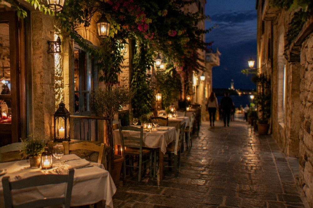 Lit restaurant tables and lanterns on a narrow stone street in the Old Town of Chania at night