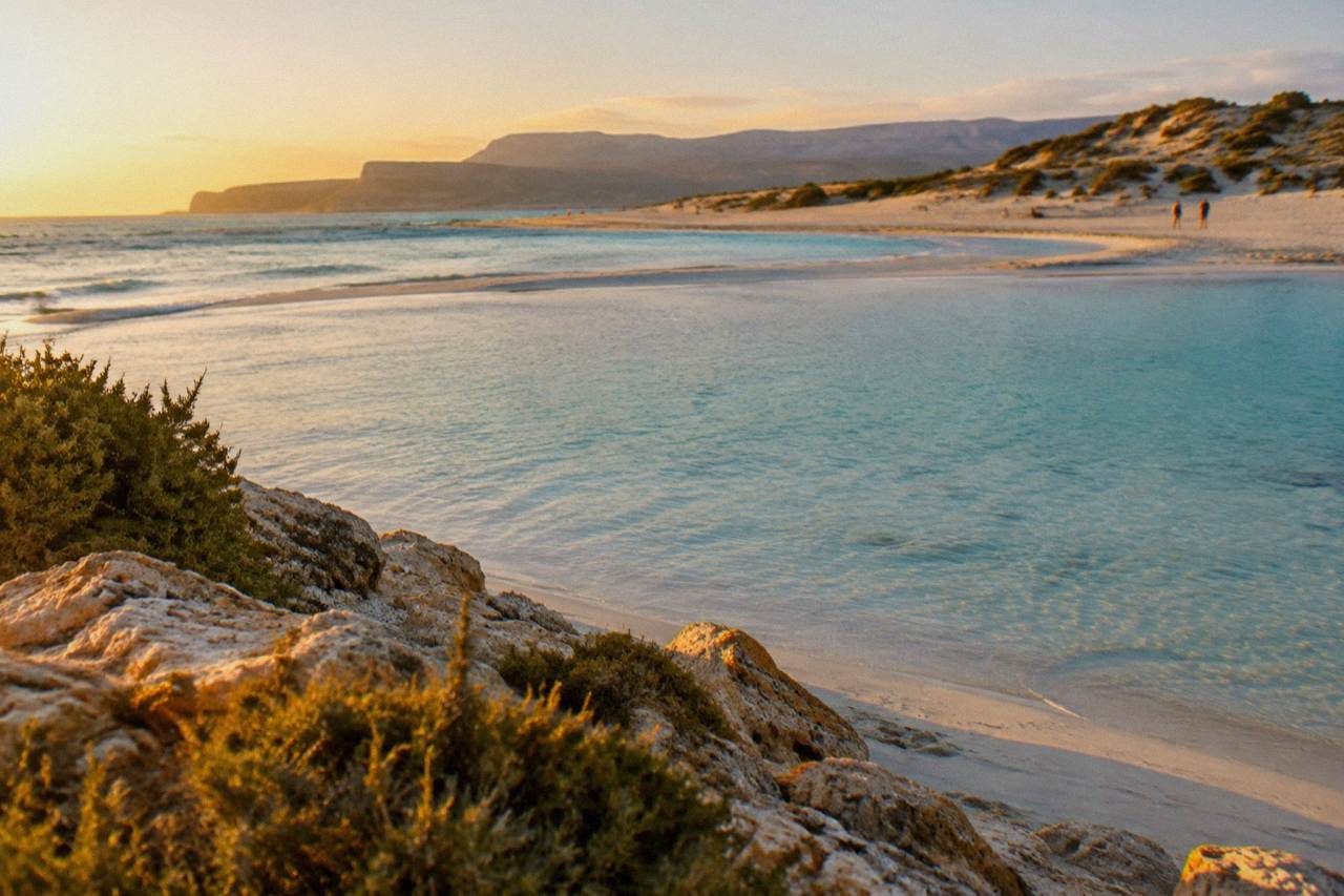 A wide shallow lagoon with pale sand and turquoise water, dunes rising behind the beach