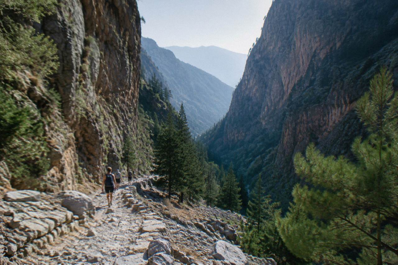 Hikers on a stony path winding down through a deep gorge with cliffs on both sides