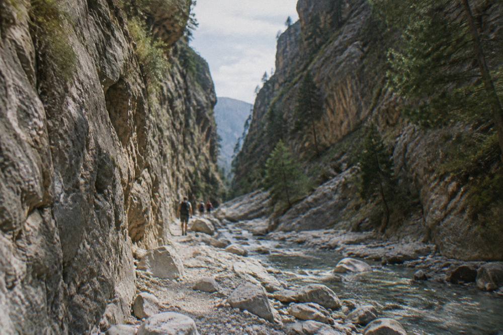 A narrow gorge passage with towering rock walls and a small stream running along the stony floor