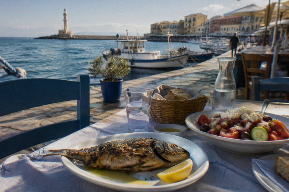 A taverna table by the water with grilled fish, salad and bread set out in daylight