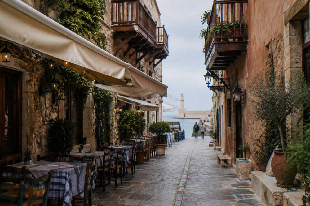 Narrow stone lanes in Chania Old Town with wooden balconies and taverna tables under awnings