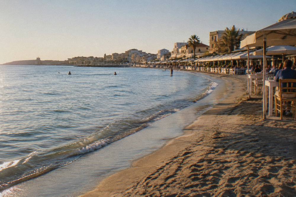 A sandy beach with calm shallow water and a line of tavernas behind it at Nea Chora