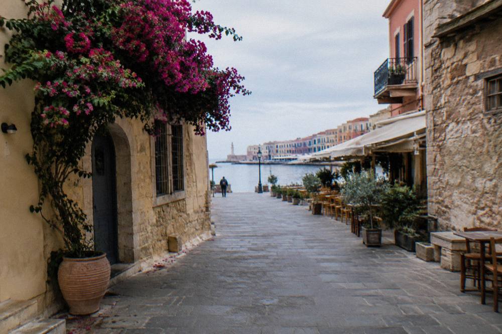 Quiet Old Town lane in Chania with pale stone walls under flat overcast light, a distant pedestrian ahead