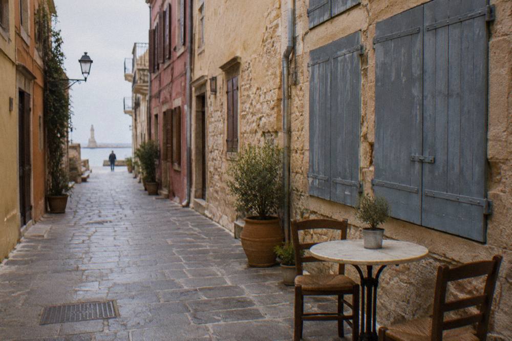 An empty stone alley in Chania Old Town with a cafe table and closed shutters on a quiet morning