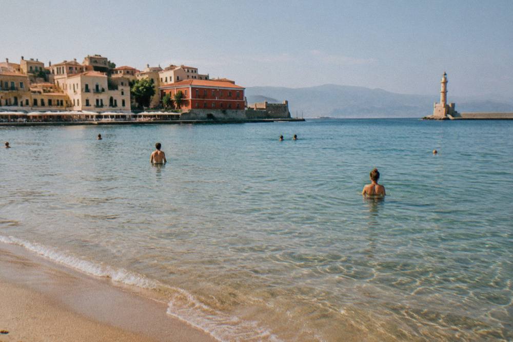 Swimmers in clear shallow water at a sandy beach near Chania on a bright calm day