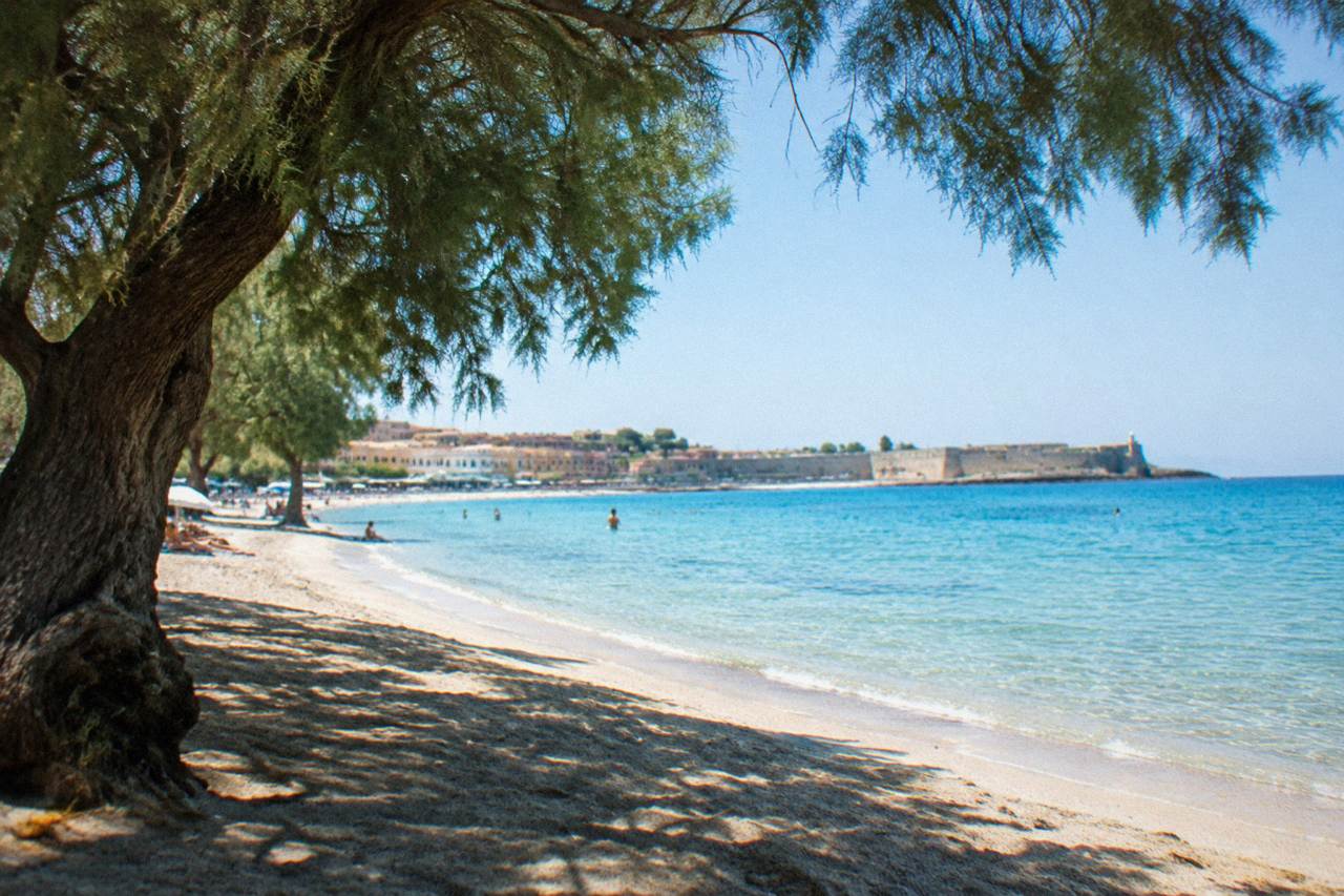 A wide lagoon of shallow turquoise water beside a pale sandy beach under a clear sky