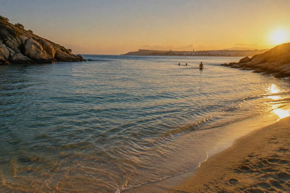 A calm sandy bay with clear shallow water and rocky headlands on either side