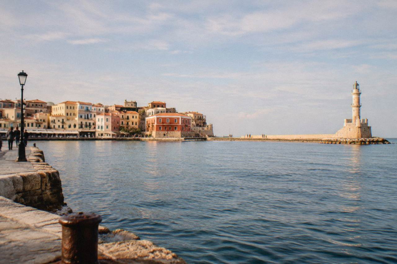 Pastel buildings of Chania Old Town rising behind the Venetian Harbour with the lighthouse at the end of the mole