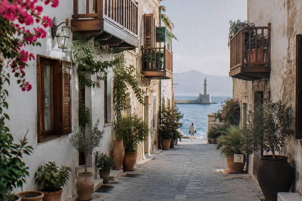 Narrow stone lane in Chania Old Town with wooden balconies and potted plants against a whitewashed wall