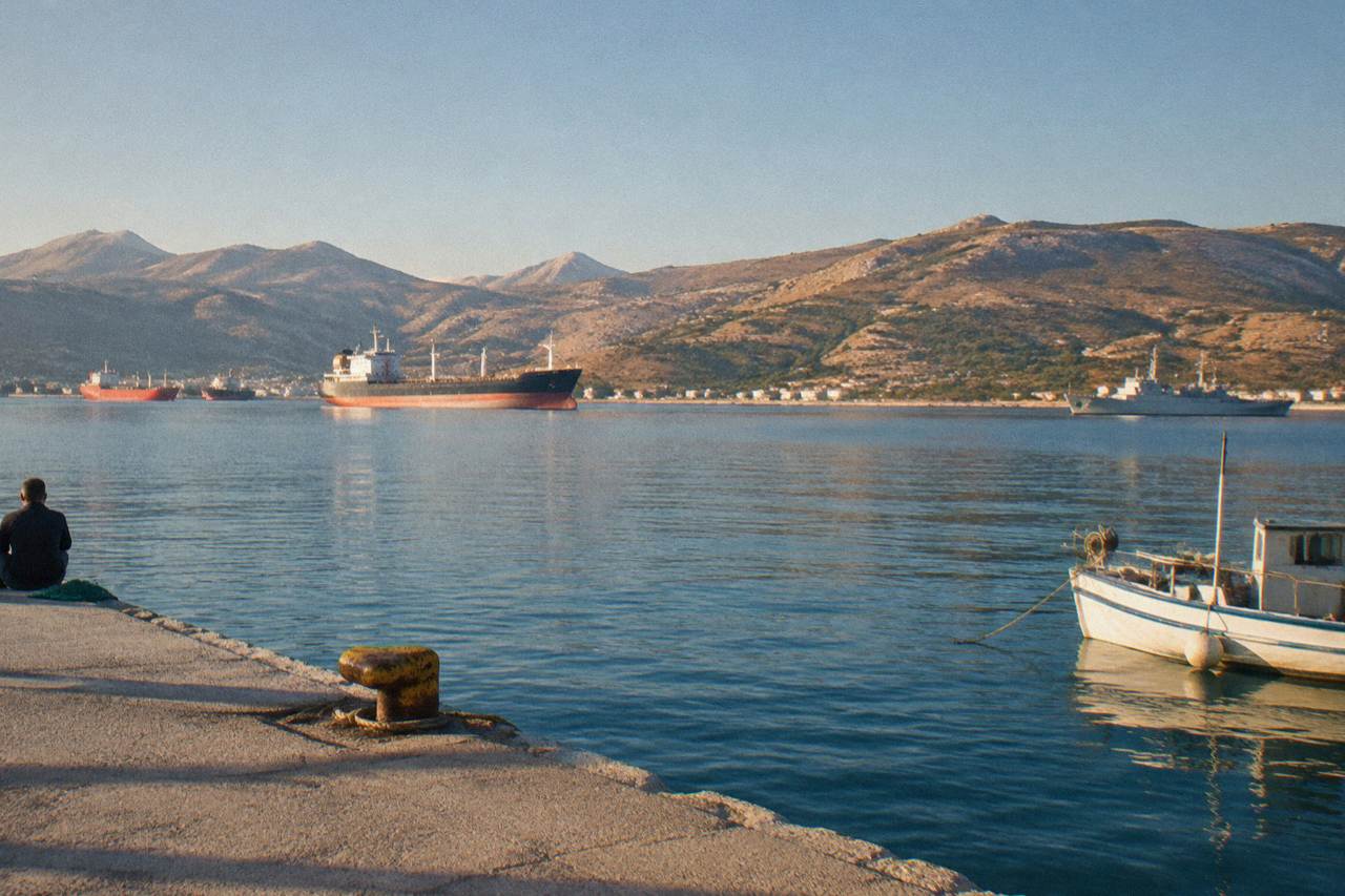 Calm bay water with anchored ships and dry hills rising behind a wide shoreline