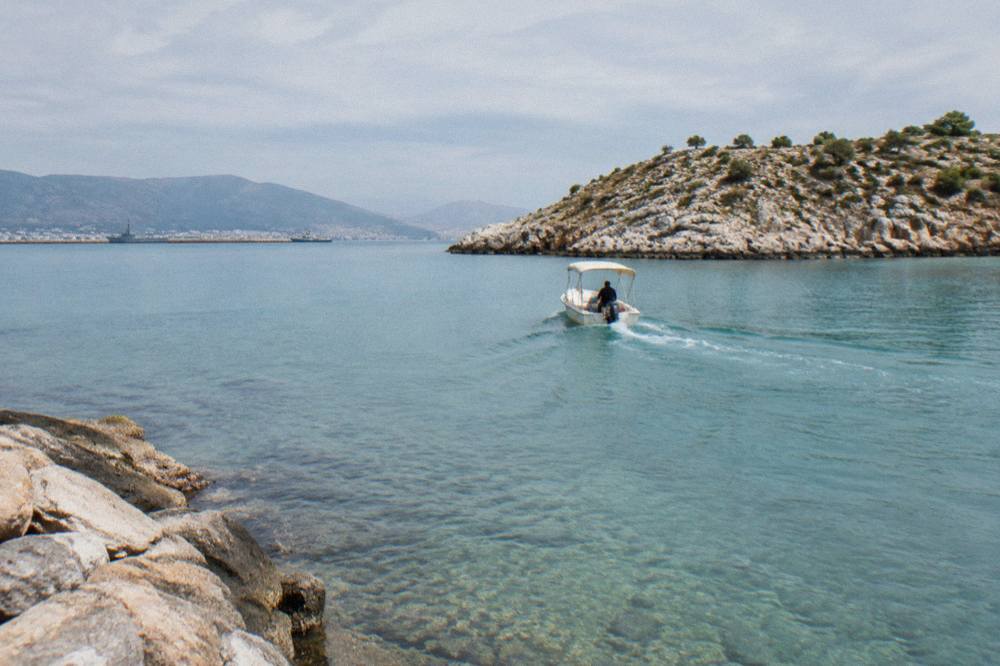 A small boat crossing clear shallow water toward a rocky headland in bright morning light