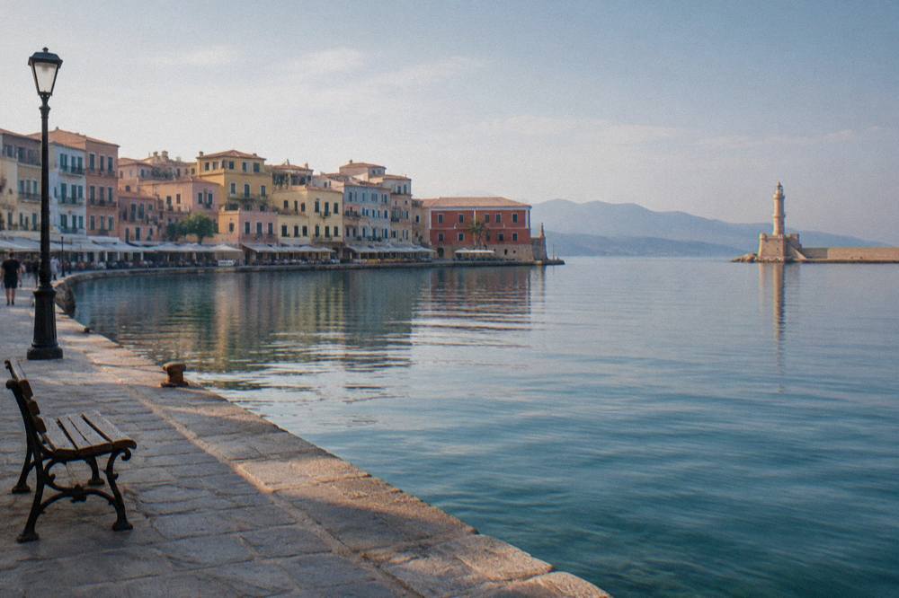 Pastel coloured buildings and a stone harbour wall along a calm seafront at midday