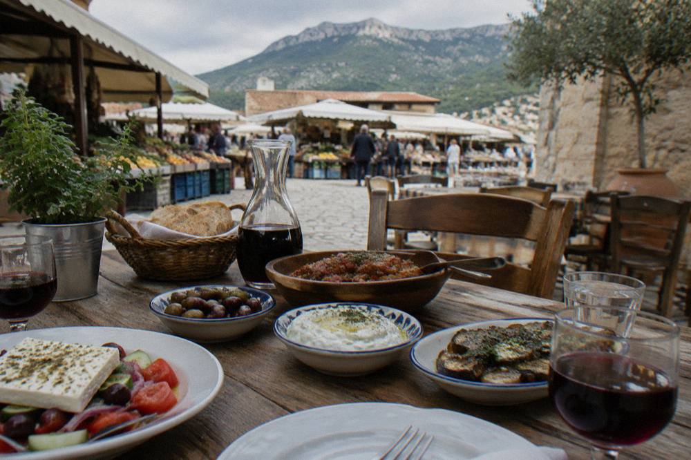 A village taverna table in the Cretan foothills set with shared dishes and a carafe of wine