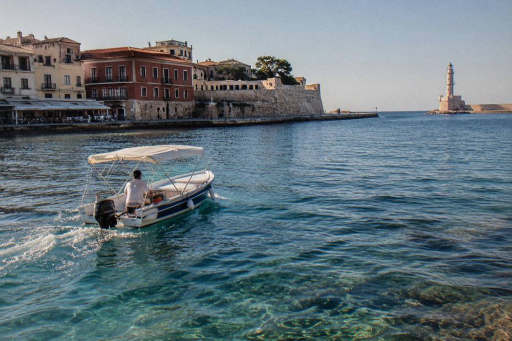 Small rental boat moving across clear shallow water near the Chania coastline