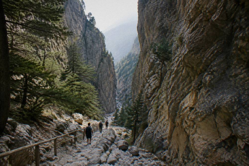 Hikers on a stony trail descending through a narrow gorge with high rock sides