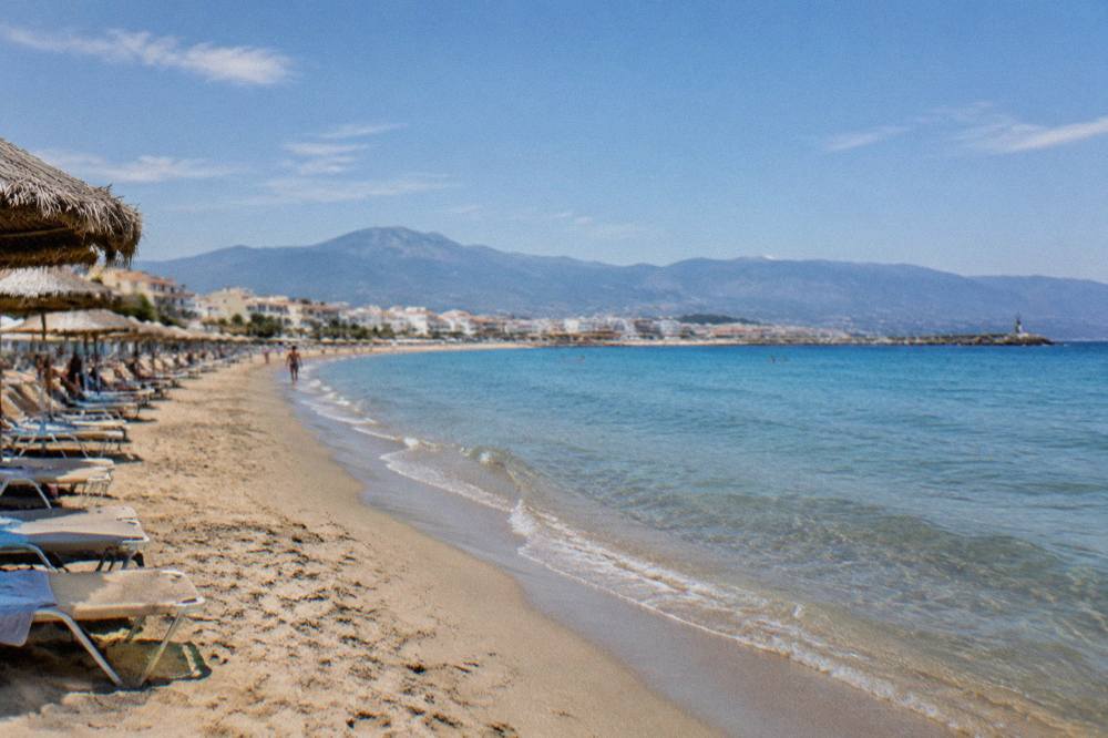 A long sandy beach with calm shallow water and sunbeds along the shore in western Crete