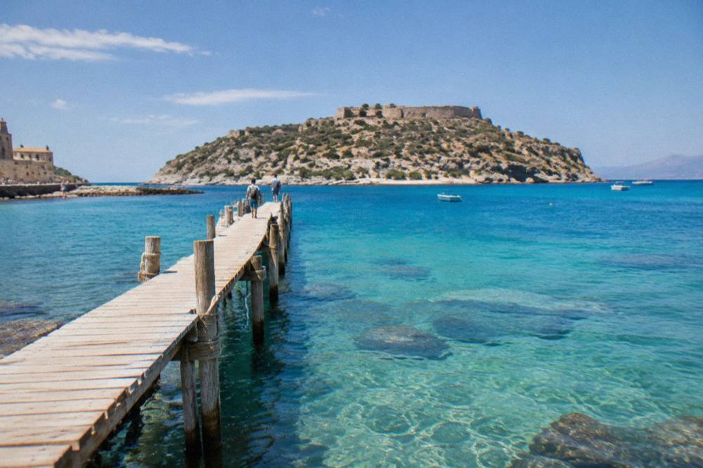 A wooden jetty over shallow turquoise lagoon water with a rocky island behind