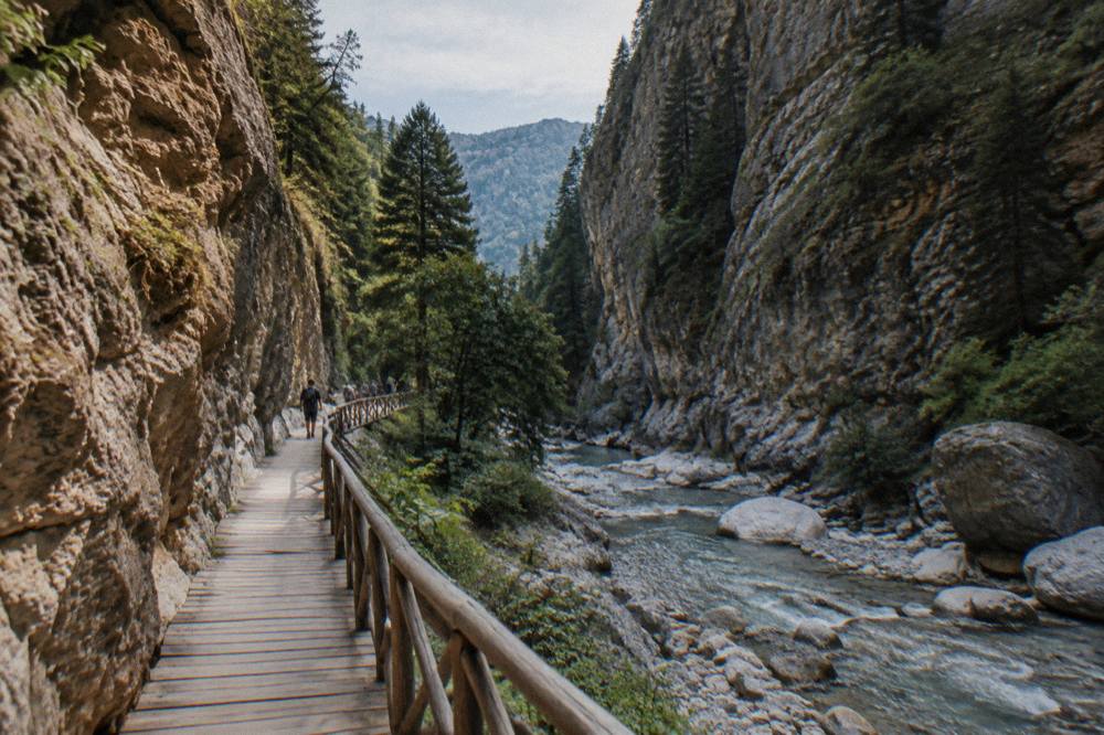 A wooden walkway along a riverbed between narrow rock walls in a green gorge