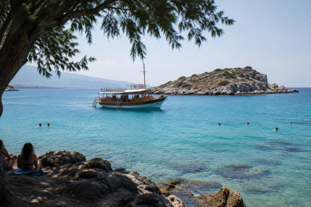 A wooden excursion boat anchored off a small rocky island with swimmers in clear turquoise water