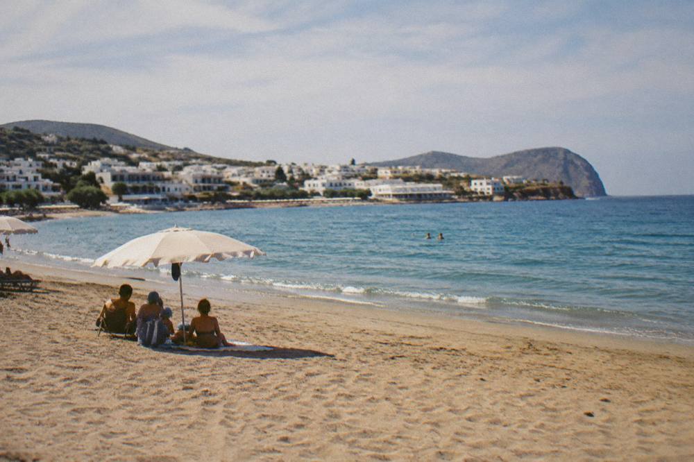 A family under an umbrella on golden sand, a calm sea and a village of white buildings behind