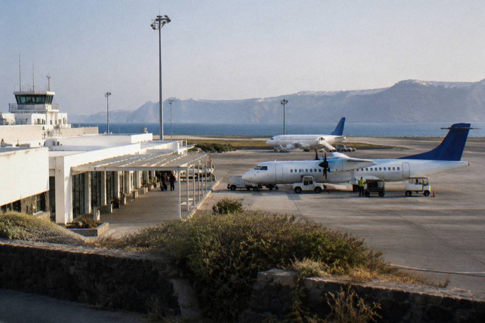 A small airport terminal building with aircraft parked on a sunny apron