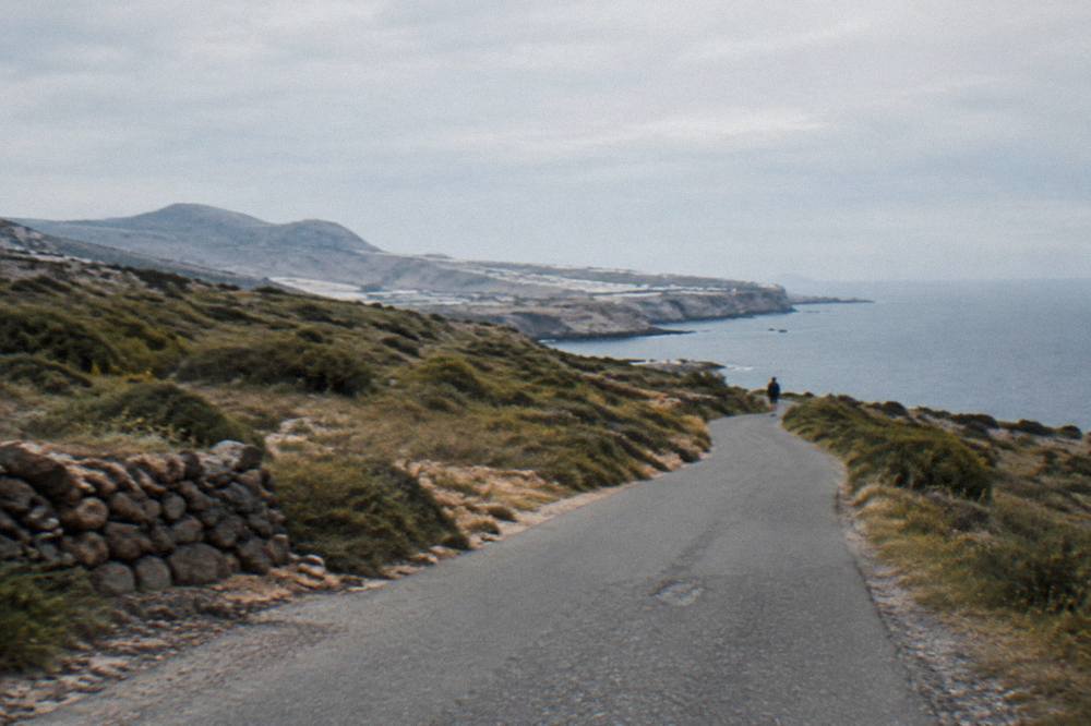 A narrow road winding through low scrub toward a distant coastline