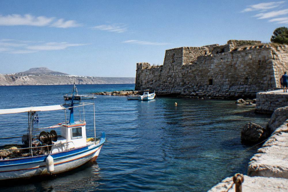 A stone fort wall at the water's edge with fishing boats moored nearby