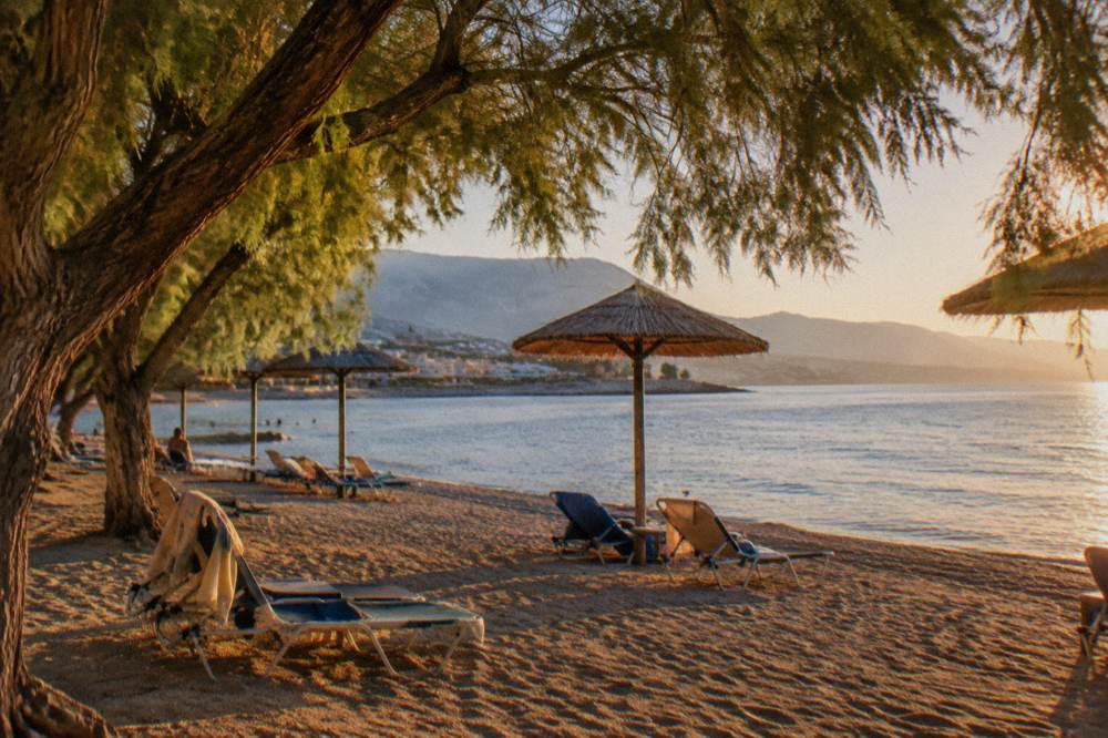 Sunbeds and umbrellas on sand under tamarisk trees beside a calm sea
