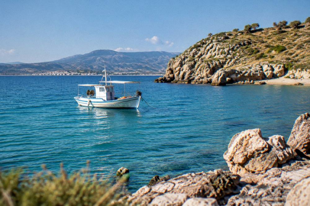 A boat anchored in turquoise water near a rocky headland at midday