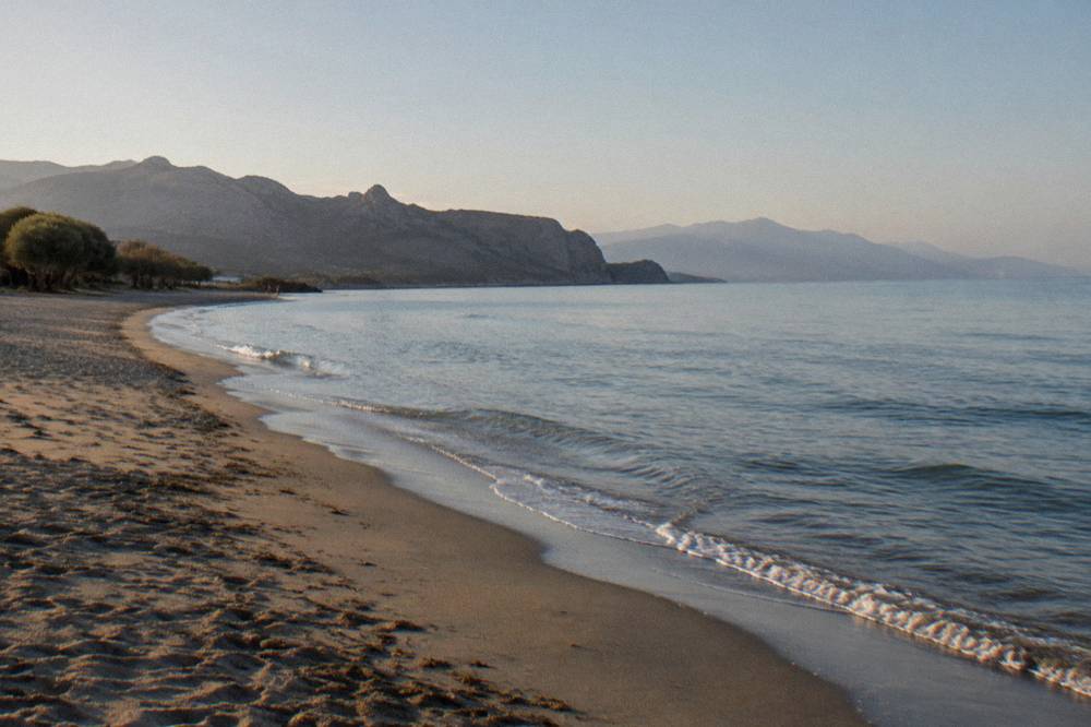 An empty curving beach with soft sand and calm water in early morning light