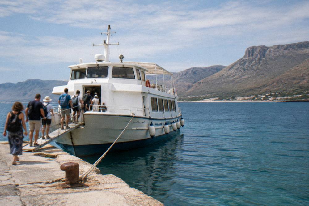 A white ferry boat moored at a small concrete pier with passengers boarding by gangplank