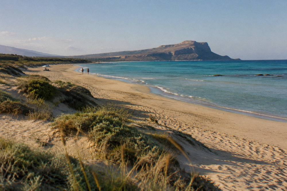 A wide sandy beach with dunes and shallow turquoise shallows stretching to a distant headland