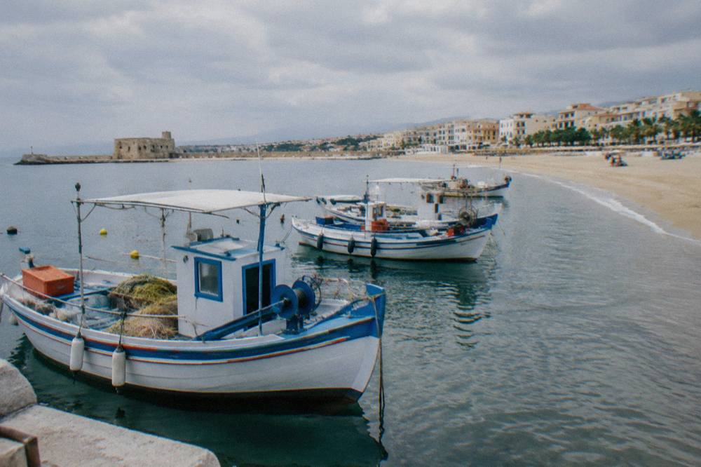Fishing boats moored in a small harbour next to a sandy beach at midday