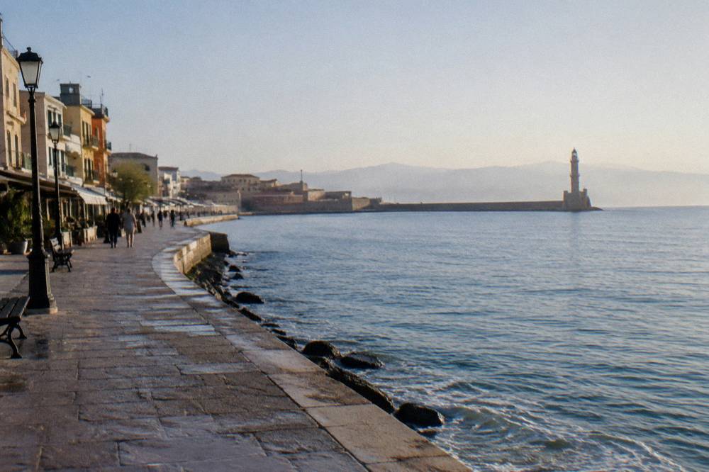 A pedestrian seafront promenade curving along the water toward a distant harbour breakwater