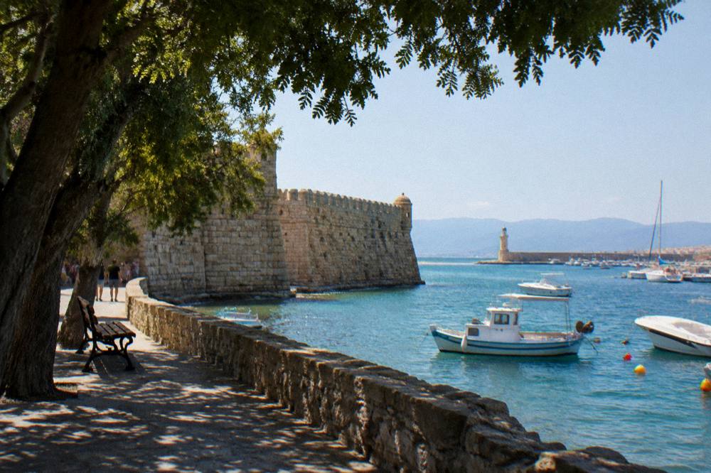 A stone fortress wall at the edge of a harbour with boats moored in the water beyond