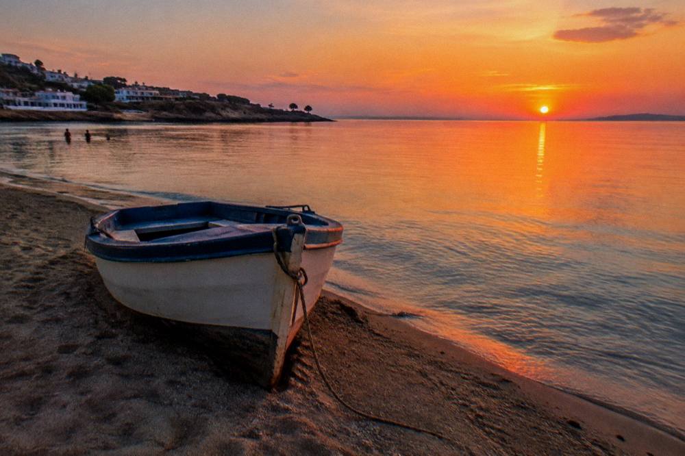 A parked small boat on sand beside clear shallow water at sunset