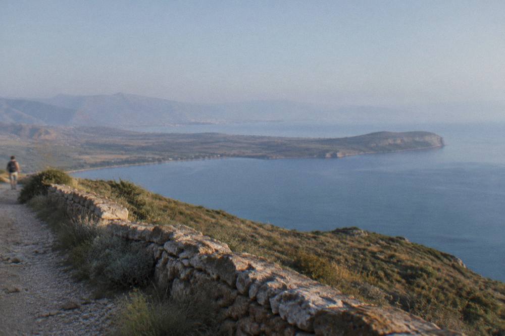 A low stone wall running along a ridge with a large bay and a peninsula beyond it