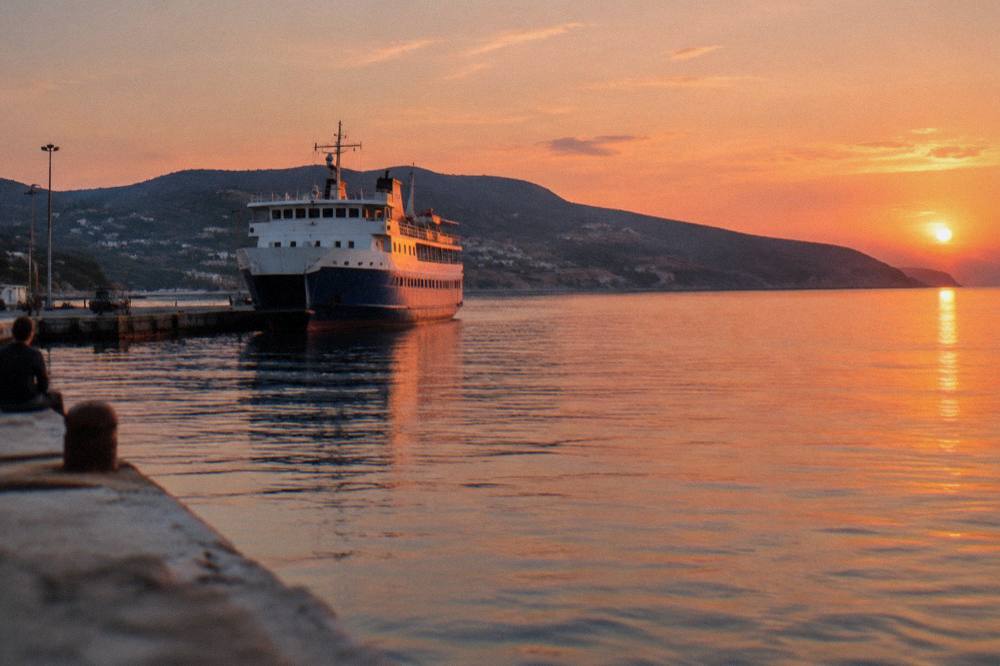 A calm harbour at dusk with a large ferry at the quay and hills behind the water