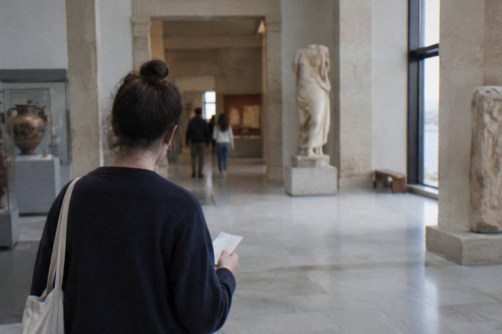 A visitor at a museum entrance hall with a paper ticket in hand, seen from behind