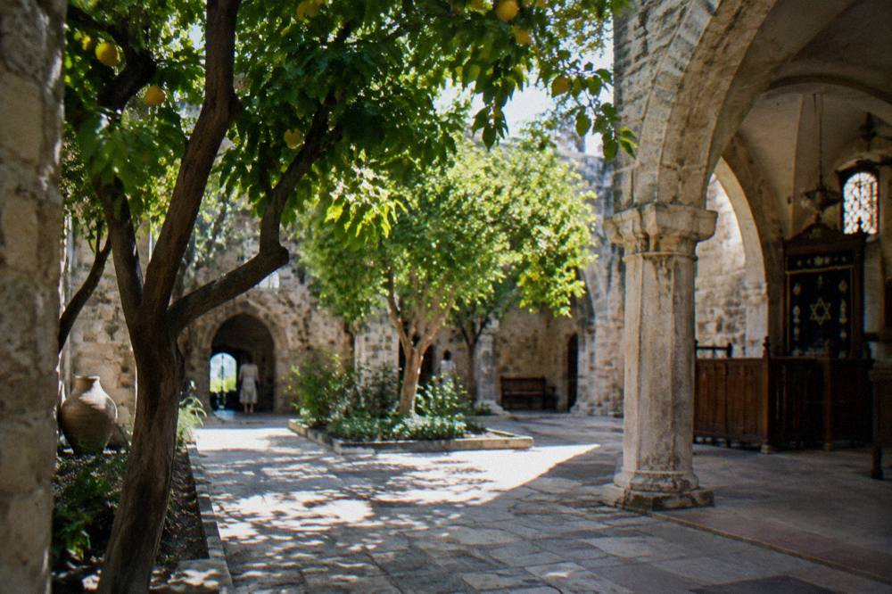 A shaded courtyard with stone paving, citrus trees and stone arches inside an old synagogue building