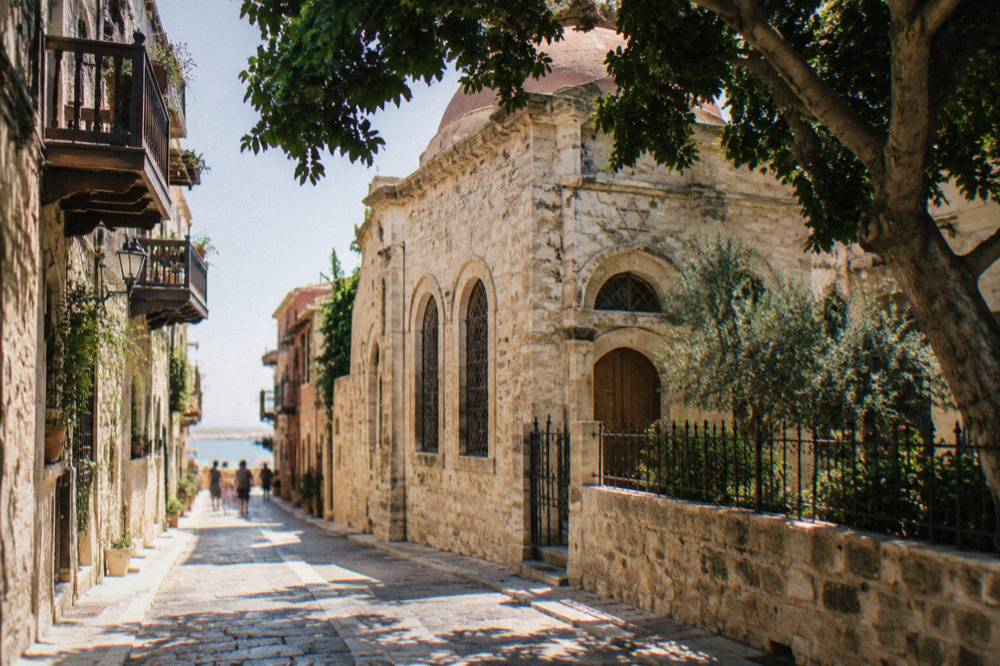 A narrow pedestrian lane in Chania Old Town with old stone walls, wooden balconies and warm afternoon light