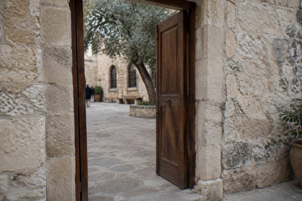 A stone doorway with a simple and an open wooden door leading into a shaded courtyard