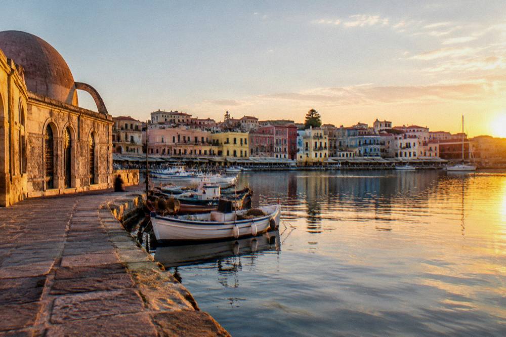 The flat waterfront of Chania Venetian Harbour seen from the mole, with pastel buildings and fishing boats in still water