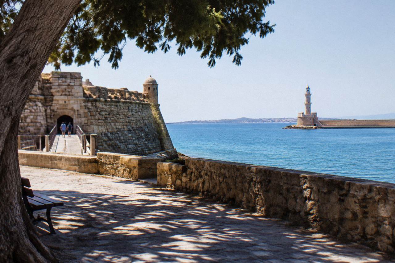 Stone fortress walls at the entrance of Chania harbour with the lighthouse across the water
