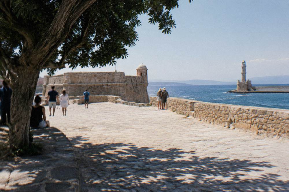 Visitors walking the open stone platform of the fortress at the tip of Chania harbour