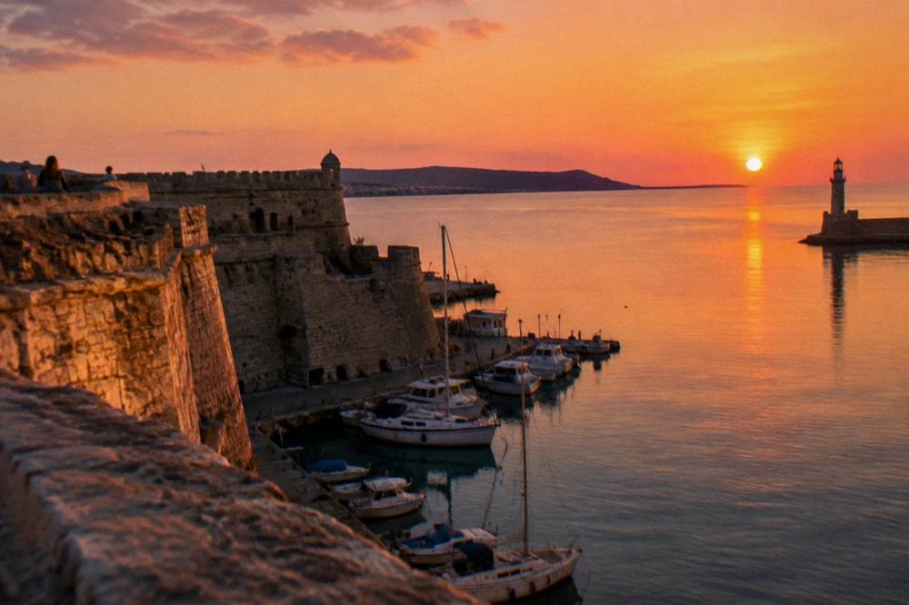 Evening light on the stone walls of the fortress with boats moored in Chania harbour below